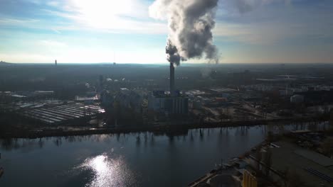 large industrial power plant emitting large amounts of smoke over the city berlin next to a river on a sunny day. fantastic aerial view flight wide orbit overview drone