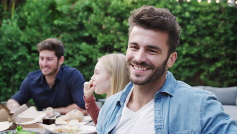 retrato de um homem com amigos em casa sentado à mesa desfrutando de comida na festa do jardim de verão