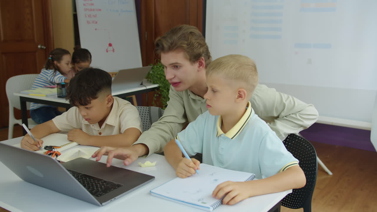 Boys Listening to Male Teacher Helping with Task on Laptop