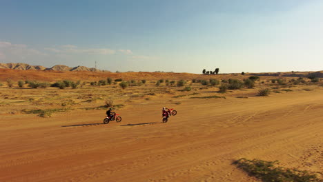 off road dirt bike riders riding together and wheeling across the desert sands during sunset