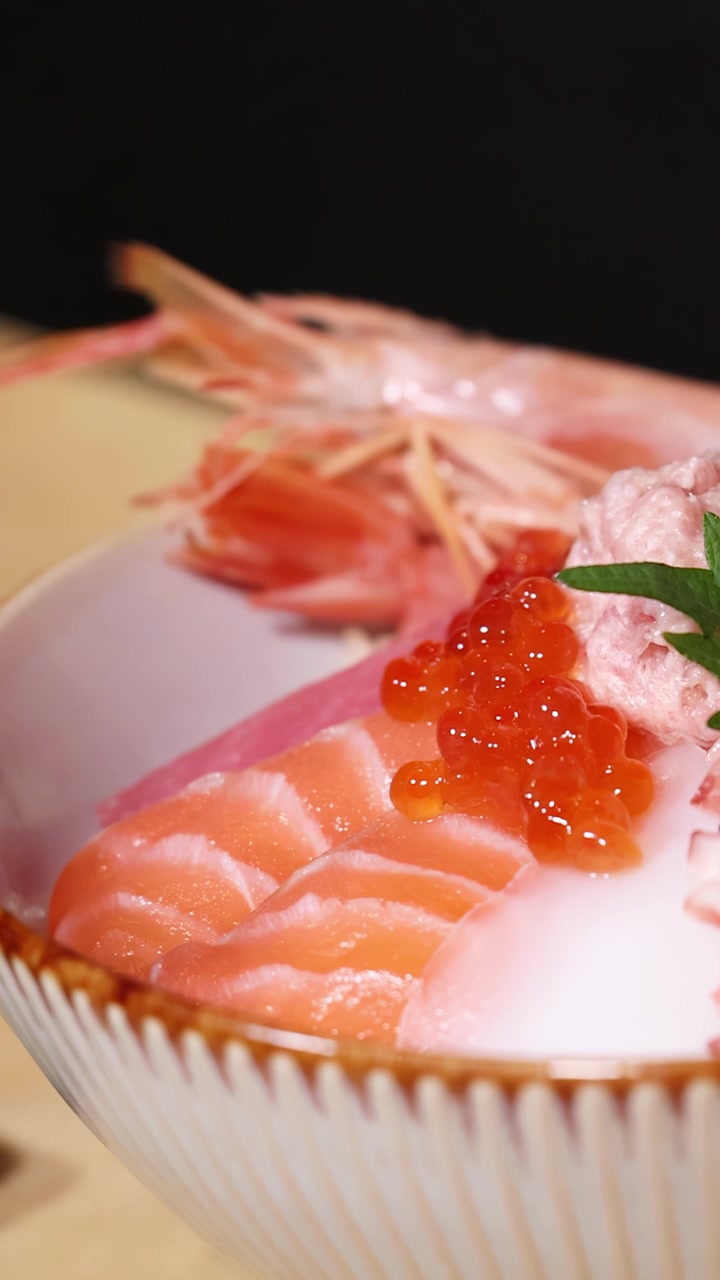 Primo piano di uno chef che aggiunge uova di salmone a una ciotola di riso colorata con frutti di mare.