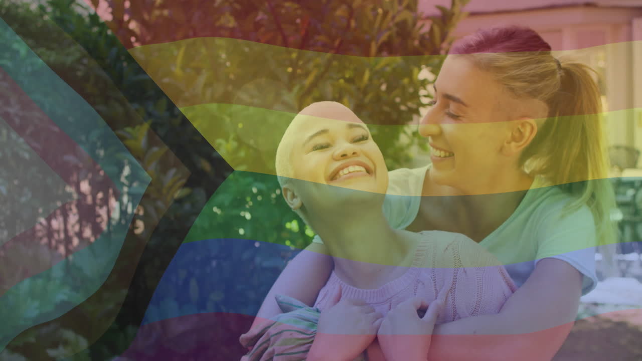 Animation of rainbow flag over diverse female couple embracing