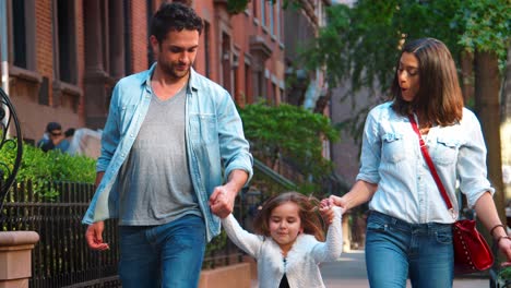 una pareja balanceando a su hija mientras caminan por la calle.