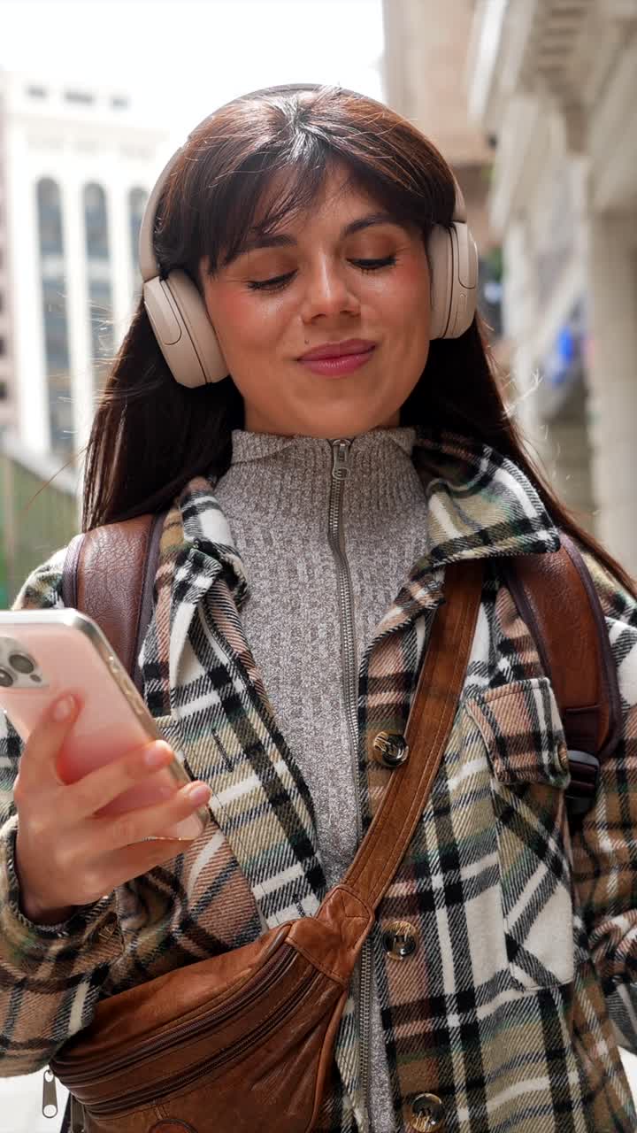 Giovane donna felice che cammina in città con le cuffie e un caffè.