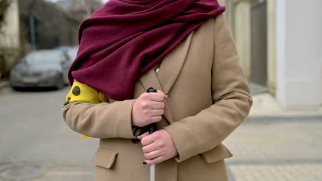 front view of unrecognizable woman in a brown coat and scarf holding a walking stick and wearing a yellow armband