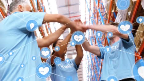 Animation-of-network-of-connections-with-icons-over-diverse-volunteers-cheering-in-warehouse