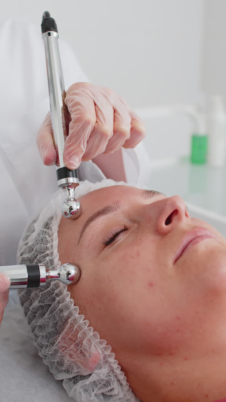 Donna di mezza età che riceve un trattamento viso e tempie con microcorrenti da un'estetista in clinica.