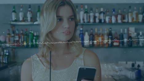 animación del procesamiento de datos sobre una mujer caucásica con una bebida usando un teléfono inteligente en un bar