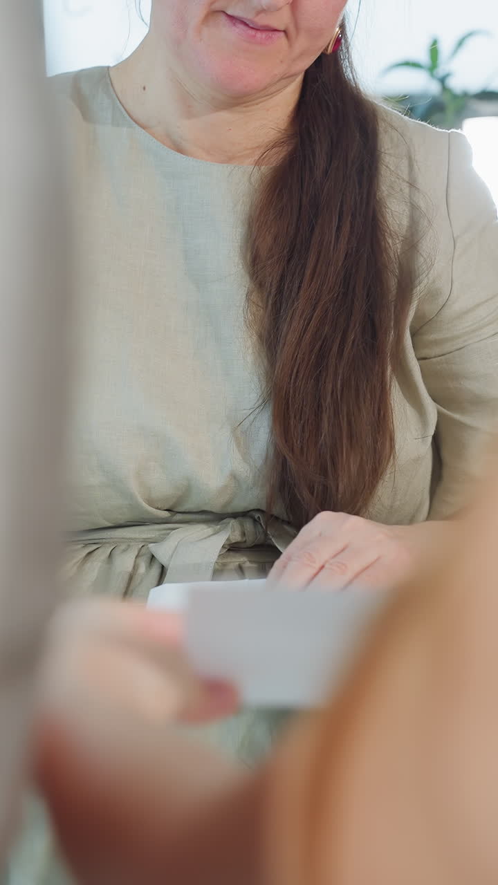 Kaukasisk mor sorterer studiekort ved bordet, rolig instruktionsstemning, hænder organiserer materialer, tålmodig tilstedeværelse som underviser, hjemmeundervisning i stuen, guidet aktivitet med børn, varmt naturligt