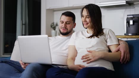 hermosa mujer embarazada y un hombre viendo una película de comedia en una computadora portátil