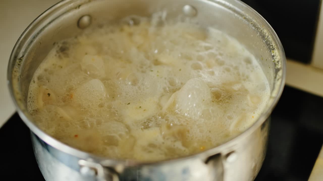 Brodo schiumoso che bolle lentamente mentre i ravioli turbinano nel liquido saporito e caldo, primo piano