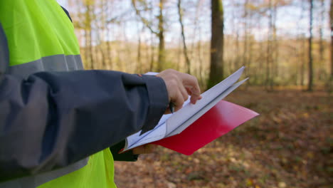 Male-worker-looking-through-his-notes-on-the-clipboard-in-the-middle-of-the-forest,-low-angle-closeup