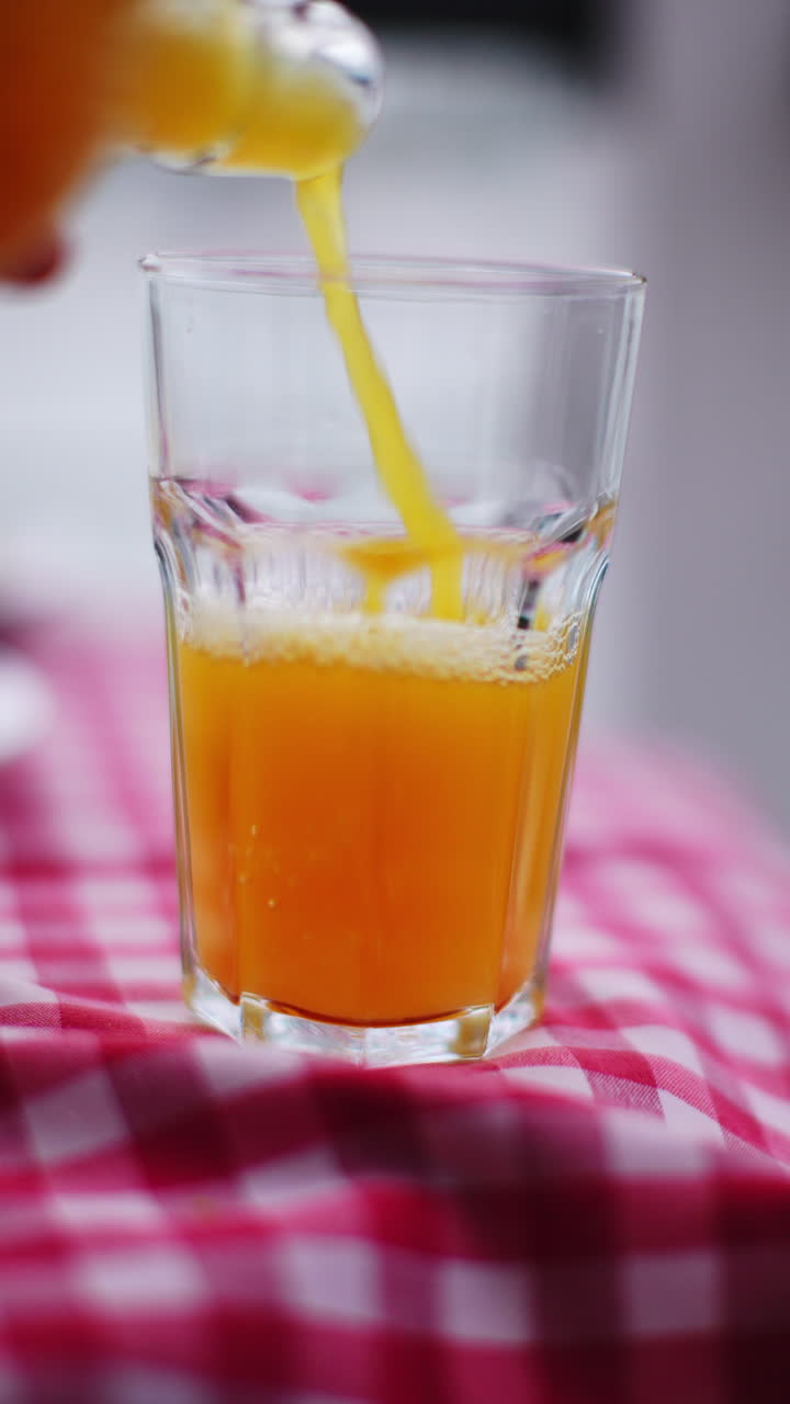 Glass of fresh orange juice being poured on red checkered tablecloth