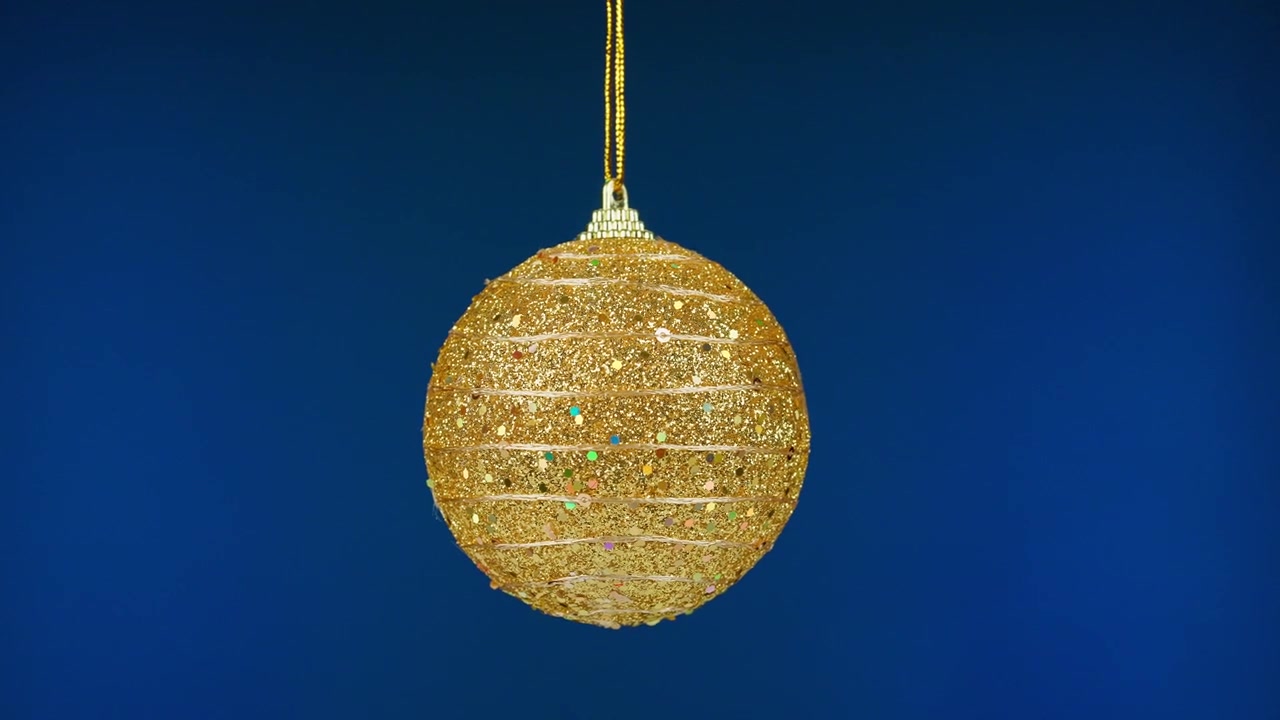 Funkelnde goldene Weihnachtskugel hängt vor blauem Hintergrund