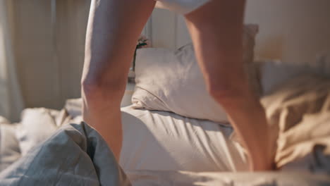 closeup legs jumping bed in morning sunlight. excited woman dancing in pajamas