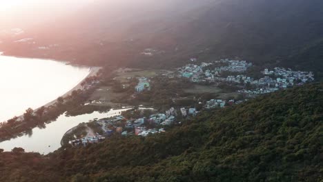 paralaje aéreo de la bahía de la playa de pui o y el mar cerca del pueblo encerrado en las colinas de la selva tropical a la hora dorada, la isla de lantau, hong kong, china