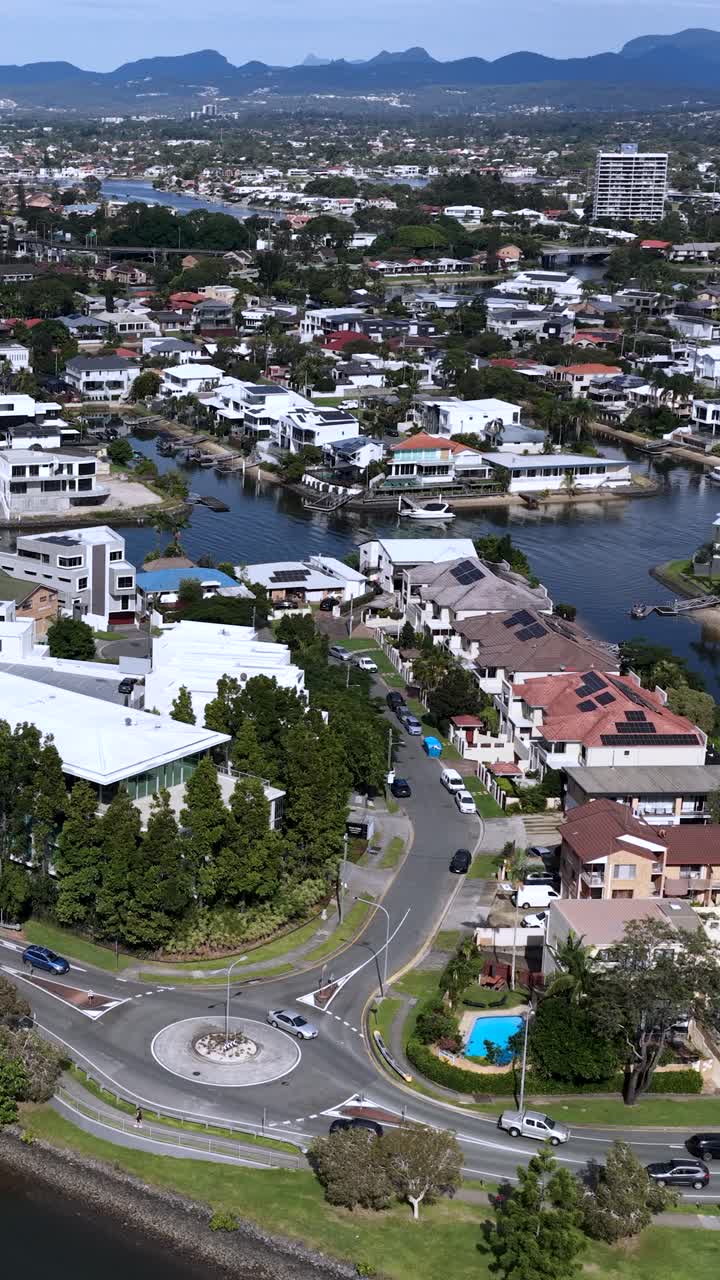 Imágenes aéreas capturan una rotonda concurrida en Gold Coast, Australia, rodeada de casas suburbanas y vías fluviales bajo la luz del día brillante