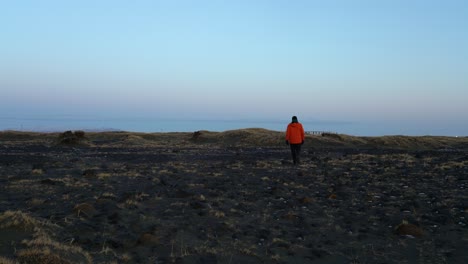 un hombre con una chaqueta naranja de invierno se aleja hacia la costa del océano - toma estática