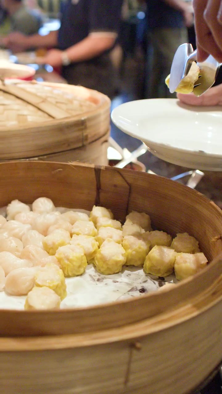 Close-up shot of a person picking yellow shumai dumplings from a bamboo steamer basket