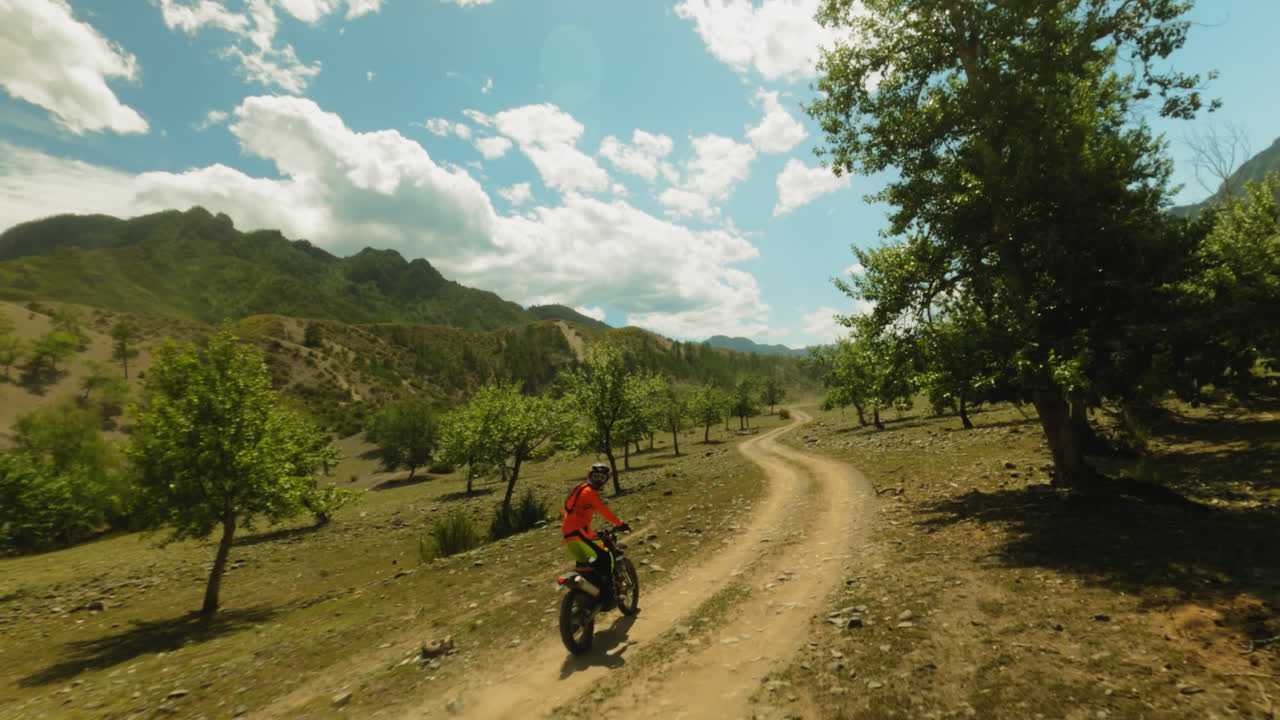 Man stands riding motorcycle across young wood fpv. Trained biker in red jacket maneuvers motorbike travelling at highland countryside. Motocross lifestyle