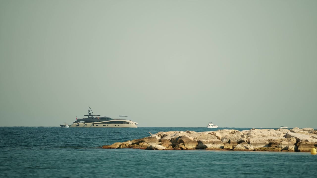 Yacht di lusso che naviga sull'oceano calmo con un vasto cielo limpido sopra, rocce in primo piano, a rappresentare viaggio e tempo libero.