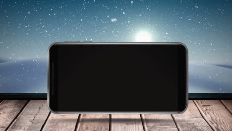 digital animation of smartphone on wooden surface against snow falling on winter landscape