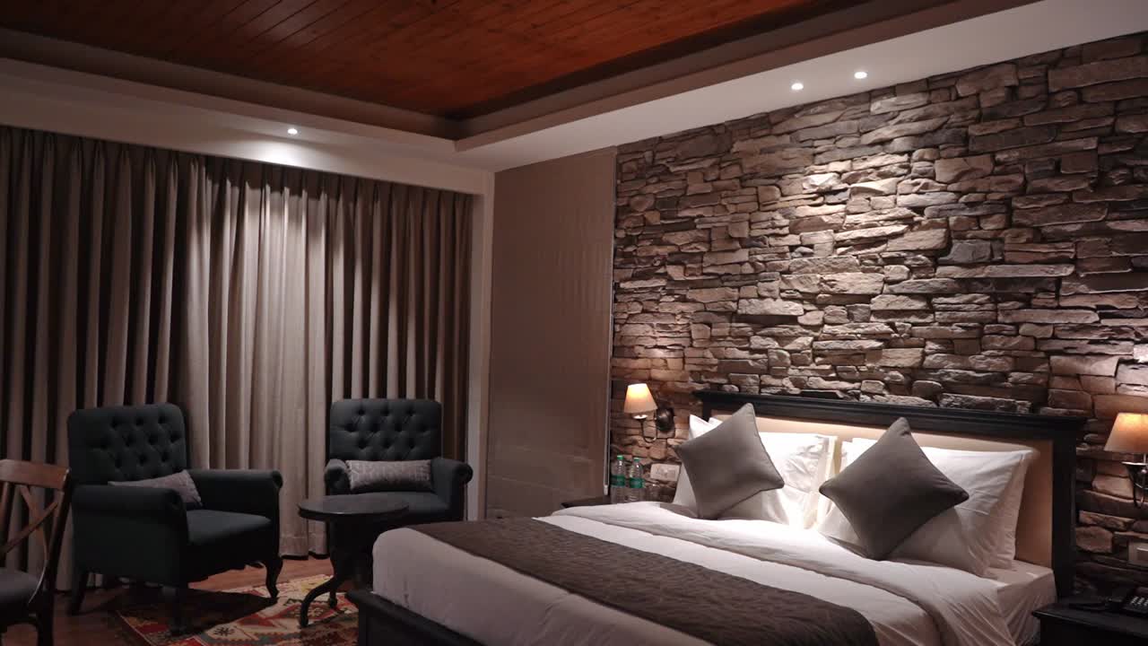 Hotel Room Interior - Luxurious Hotel Suite With Comfortable Bed Against Stone Accent Wall And Two Tufted Chairs On The Side - revealing shot