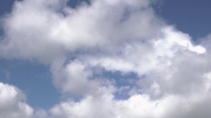 Soft white clouds drift across a bright blue sky, creating a peaceful natural background with airy daylight atmosphere.