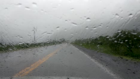 raindrops on the windshield while driving in heavy rain, low grey clouds hang above the wet road