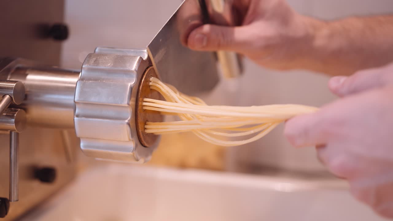 남성 요리사가 동행하여 파스타 기계에서 스파게티의 긴 가닥을 자릅니다.