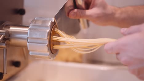 male cook accompany and cuts the long strands of spaghetti from the pasta machine