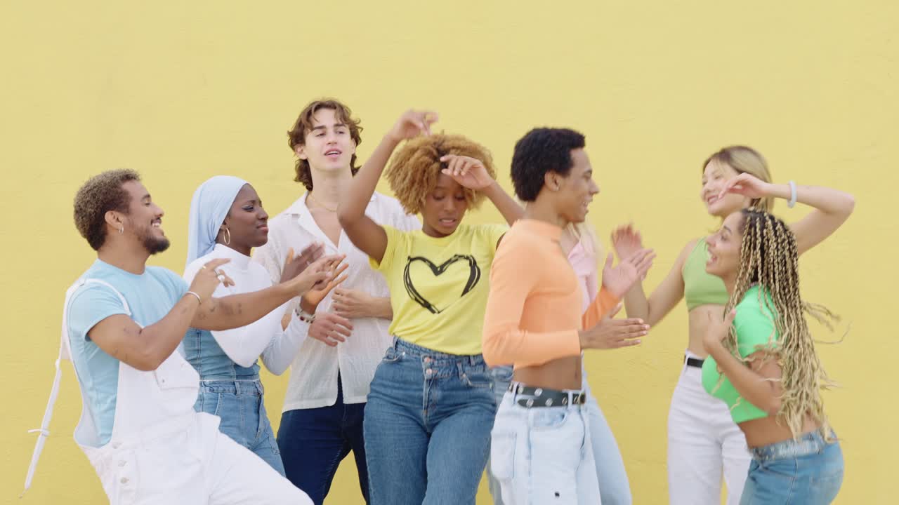 A group of diverse friends dancing in front of a yellow wall