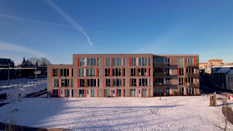 backwards aerial of exterior facade residential housing at the ettegerpark during sunrise after a snowstorm with ettegerpark covered in snow