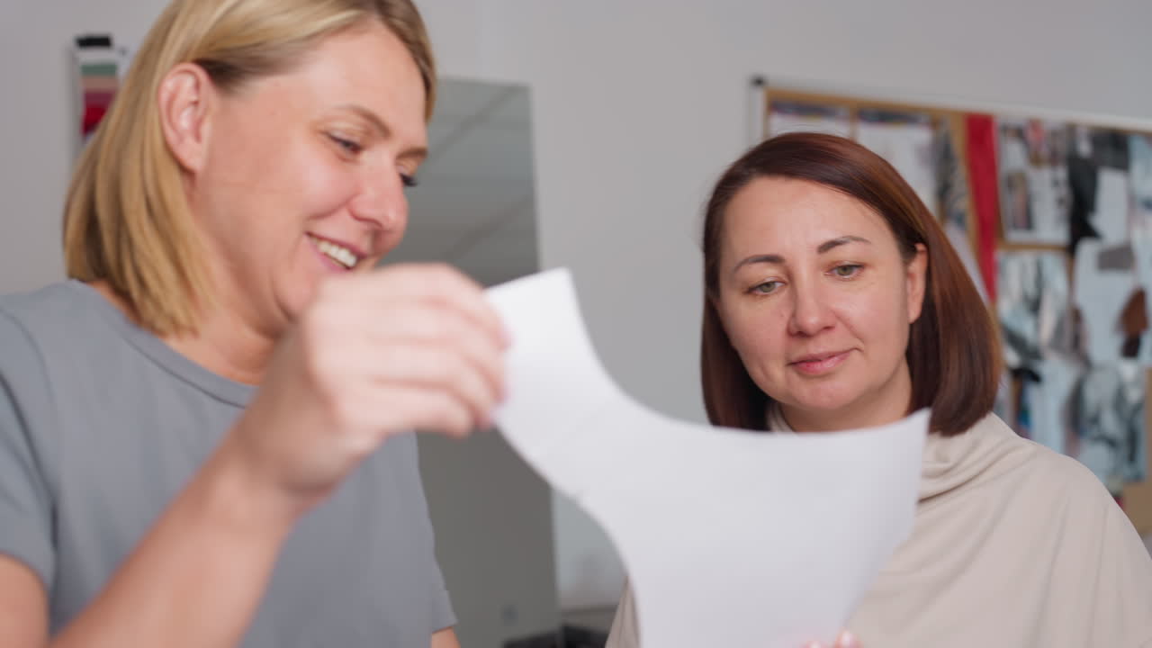 Clothing designers engaged in collaborative discussion while carefully observing material sample in bright workspace, sharing ideas and planning project together with creative energy
