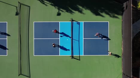 two teams playing pickleball outside, birds-eye aerial view from above on blue clay court