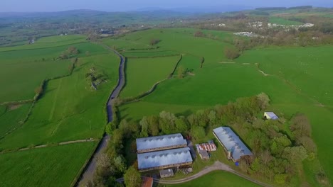 Aerial-drone-shot-of-modern-farm-building-following-a-country-lane-in-Summer