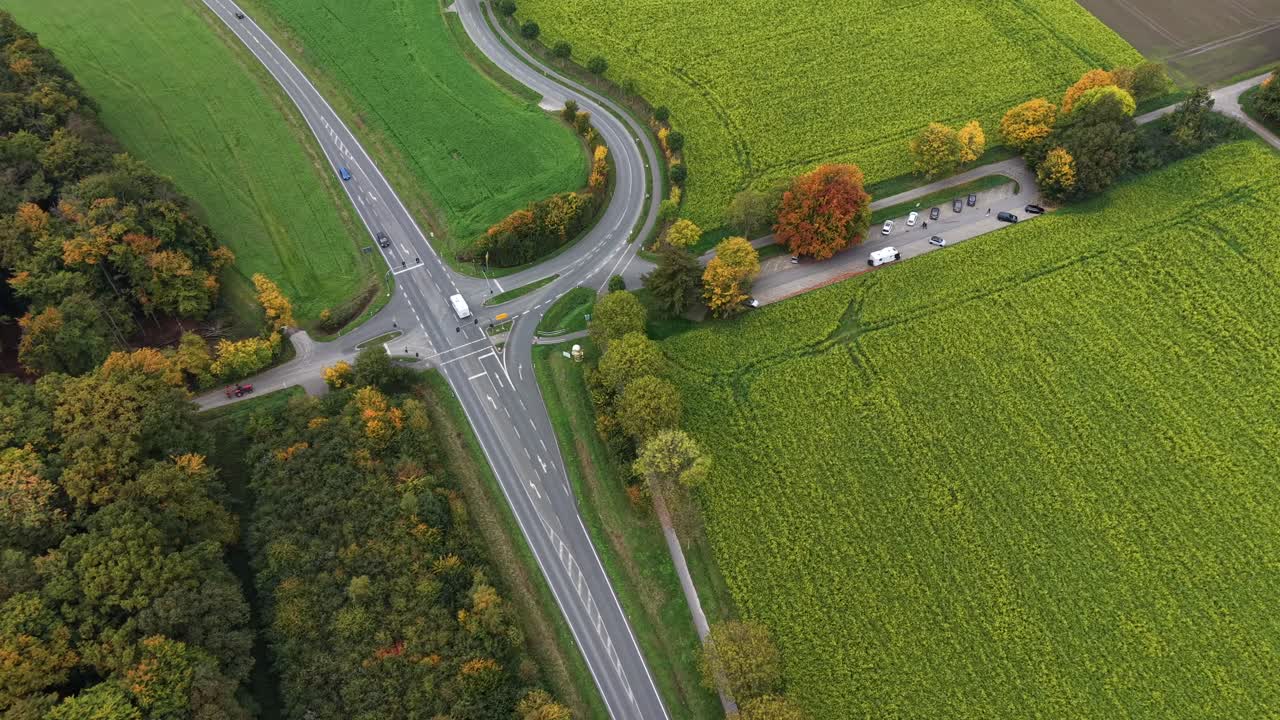 Rural American road intersection surrounded by green fields and vibrant autumn foliage, with cars parked along a countryside lane during fall season. aerial top down shot. Traffic scene suburbia