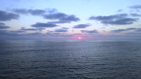 low light scenic sunset above vast open ocean with several clouds in sky, aerial