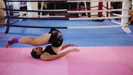 Fitness-woman-doing-abdominal-crunches:-she-raises-her-legs-up-then-moves-them-behind-her-head-inside-of-the-boxing-ring-in-a-gym.-Shot-in-4k