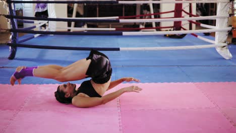 mujer de fitness haciendo abdominales: levanta las piernas y luego las mueve detrás de su cabeza dentro del ring de boxeo en un gimnasio. filmado en 4k