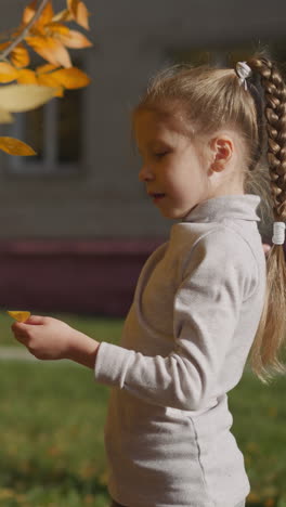 aunt with disability and little niece have fun in autumn park. young woman and preschooler girl examine bright yellow dried leaves and play together happily closeup