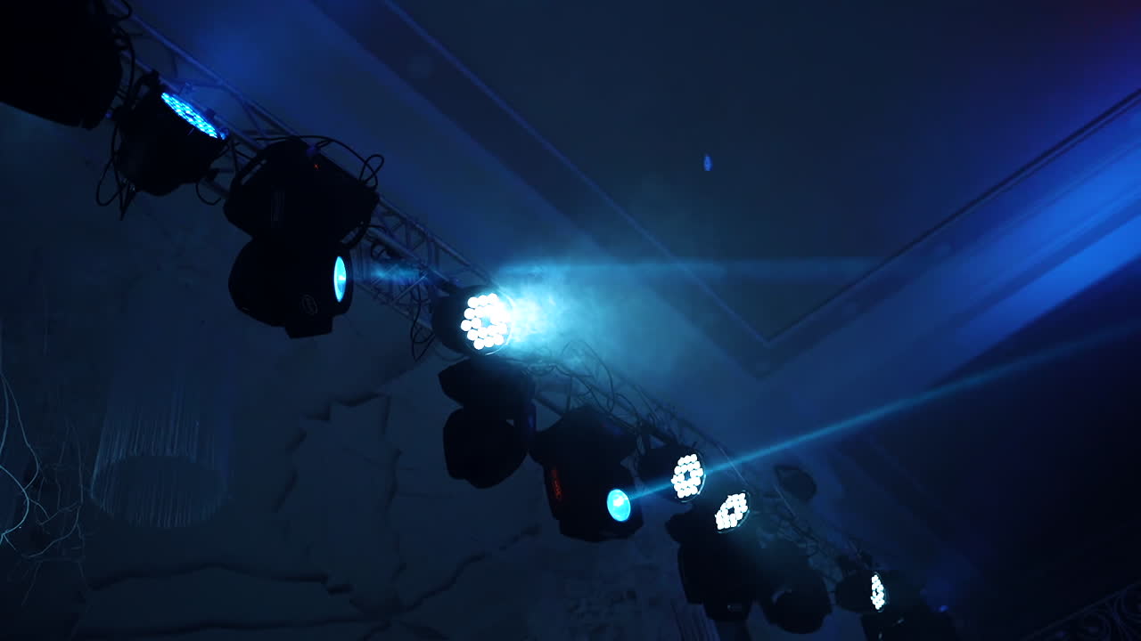 Colorful spotlights on the dark background. Different projectors spinning and glowing with laser rays inside the dance club. Led lighting equipment.