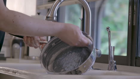 a caucasian male is cleaning a cooking pan in a home kitchen