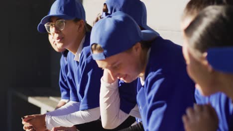 grupo diverso de jugadoras de béisbol sentadas en el banco escuchando al entrenador