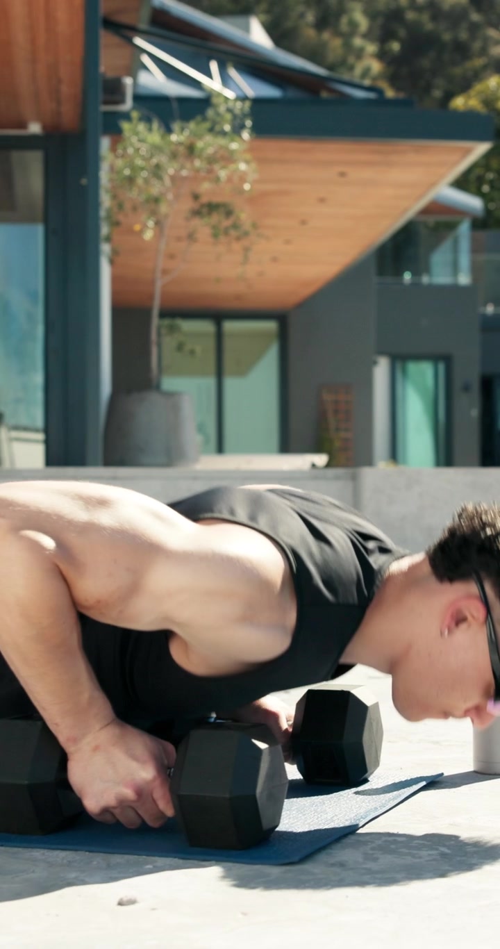Young Man Doing Push-Ups with Dumbbells Outdoors