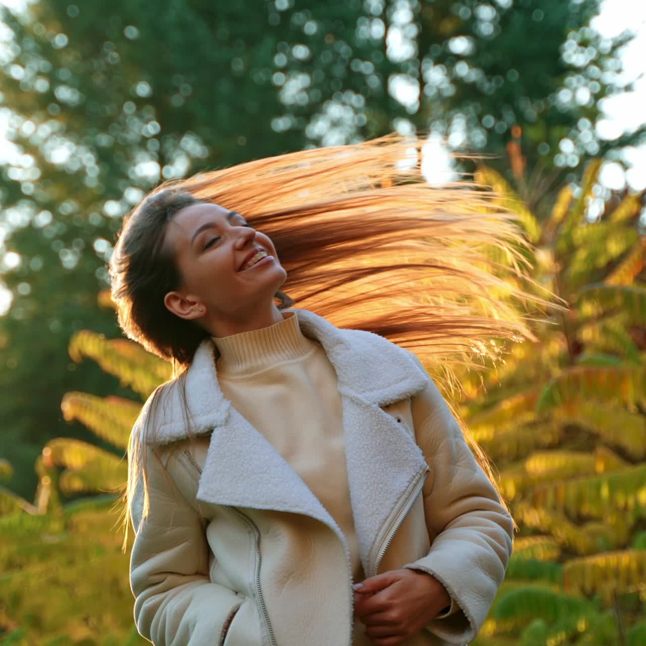 Beautiful smiling lady in light warm clothes waving hair in the rays of setting sun. Woman spending time outdoors on nice autumn day