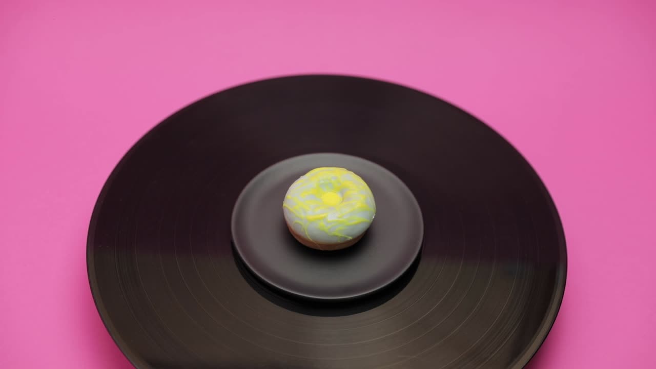 An American donut topped with blue chocolate with yellow choco lines turns in a circle on a black turntable. The shot from above