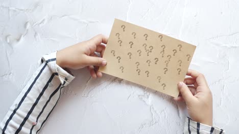 child's hands holding paper with question marks