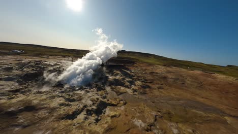 aerial fpv shot of tourists standing beside a steam cloud from a natural spring