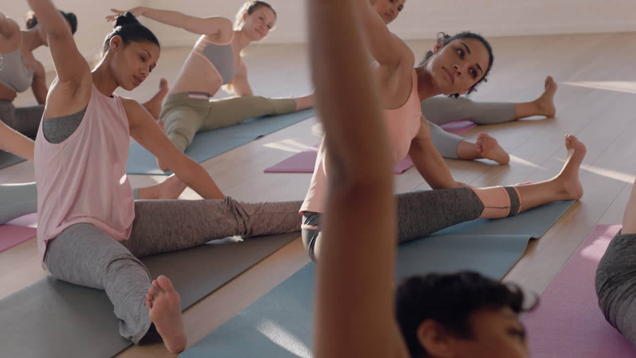 yoga-klasse mit schönen multiethnischen frauen, die sitzende seitenbeuge-pose üben und einen gesunden lebensstil genießen, indem sie im fitnessstudio gruppenmeditation bei sonnenaufgang ausüben